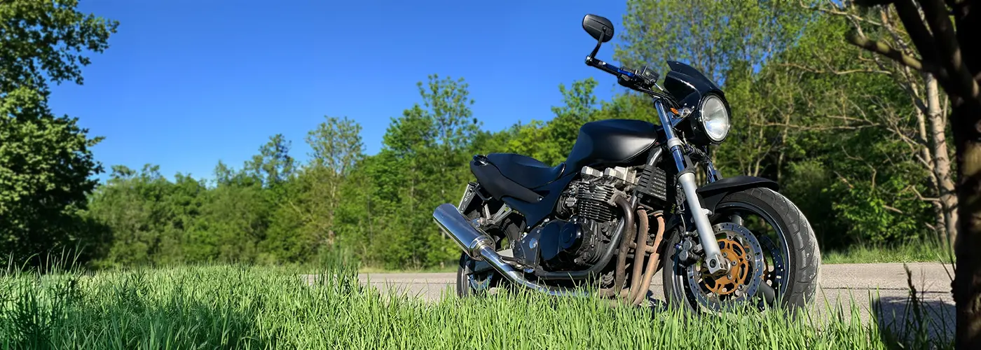 Schwarze Kawasaki in Naked Bike Optik aus der Froschperspektive im Grünen bei blauem Himmel - freie Motorradwerkstatt MotoPassion bei München