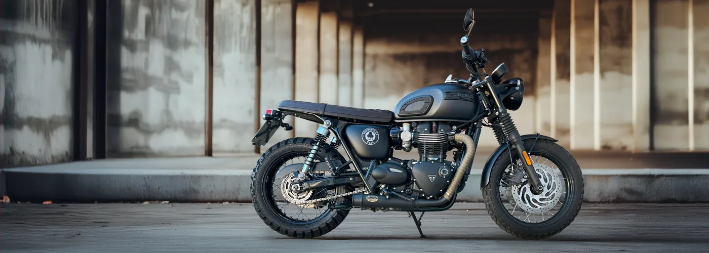 Triumph Bonneville T100 ACE Edition in Matt-Schwarz, seitliche Ansicht mit klassischem Zweizylinder-Motor, Doppelfederbeinen und Speichenrädern - aufgenommen bei MotoPassion in Emmering bei München.