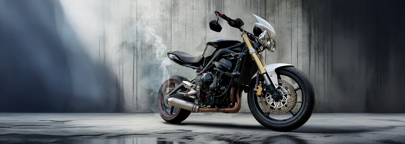 Individuell umgebautes Custom-Naked-Bike von MotoPassion in Emmering bei München mit schwarzem Bodywork, goldener Upside-Down-Gabel, Dreizylinder-Motor und sportlicher Bremsanlage vor Betonwand.