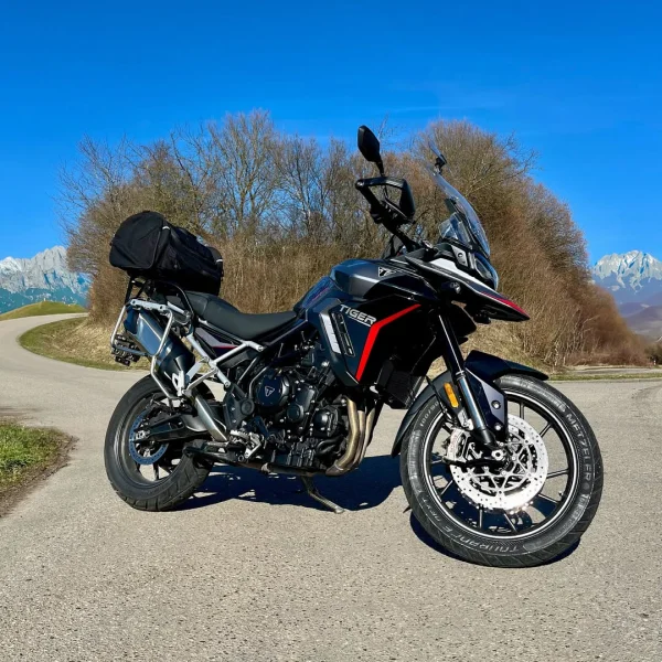 Triumph Tiger Adventure-Bike in Schwarz mit rotem Akzent, hoher Windscheibe, Dreizylinder-Motor und montierter Gepäcktasche, unterwegs nahe Emmering bei München.
